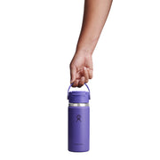 A purple Hydro Flask insulated water bottle with a matching purple carry handle, held by a person's hand against a solid white background.
