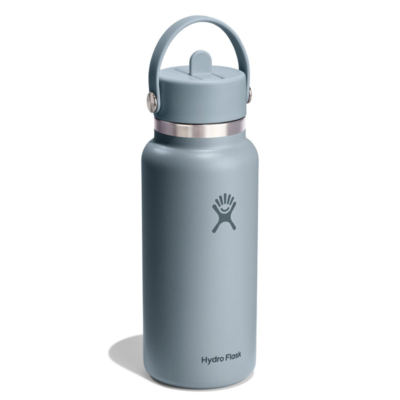 A Hydro Flask water bottle in a muted slate blue-gray color, featuring a matching blue-gray lid with a carry loop and a silver metal band near the top. The Hydro Flask logo is printed on the front, and the brand name is visible near the bottom, set against a clean white background with a soft shadow.