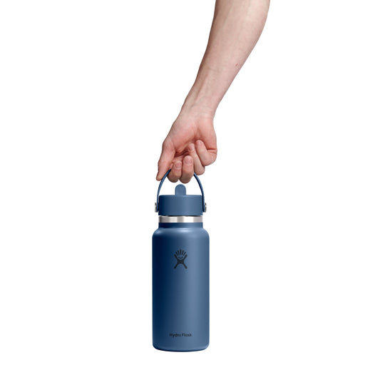 A hand holding the handle of a matte blue Hydro Flask water bottle against a solid white background.