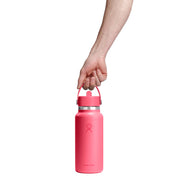 A hand holding a pink insulated water bottle with a carrying loop lid by Hydro Flask on a white background.