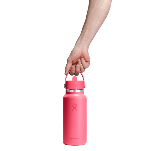 A hand holding a pink insulated water bottle with a carrying loop lid by Hydro Flask on a white background.
