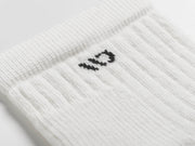 A close-up of a white ribbed knit sock with a small black embroidered logo on the side, set against a clean white background.