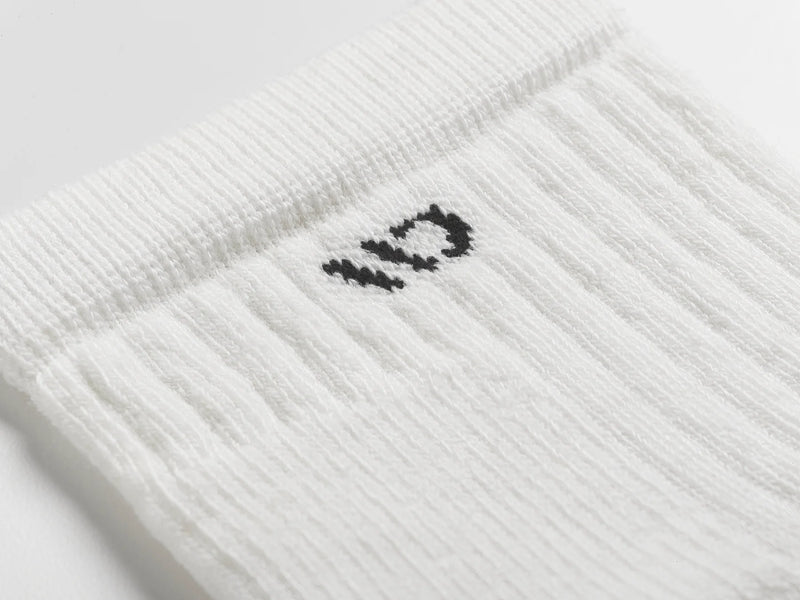 A close-up of a white ribbed knit sock with a small black embroidered logo on the side, set against a clean white background.
