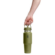 An olive green insulated water bottle with a carry loop, held by a person's hand against a solid white background. The Hydro Flask logo is visible on the front of the bottle.