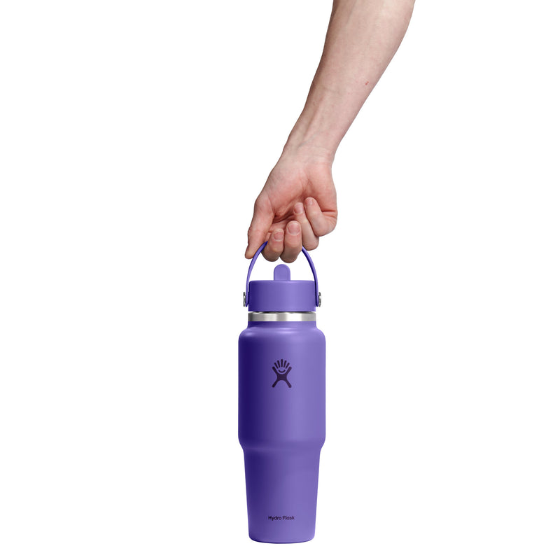 A hand holding a purple Hydro Flask insulated water bottle with a carrying loop against a solid white background.