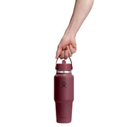 A hand holding the handle of a tall, insulated water bottle against a solid white background. The bottle is a dusty rose or mauve color with a black Hydro Flask logo on the front.