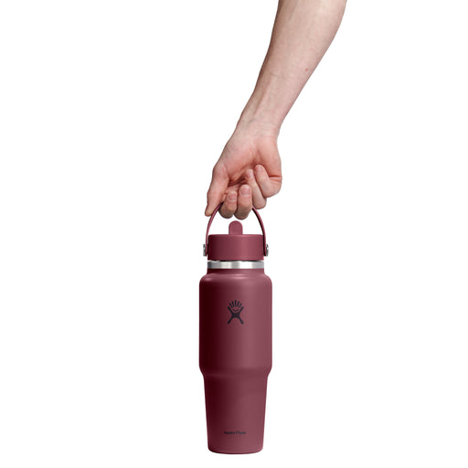 A hand holding the handle of a tall, insulated water bottle against a solid white background. The bottle is a dusty rose or mauve color with a black Hydro Flask logo on the front.