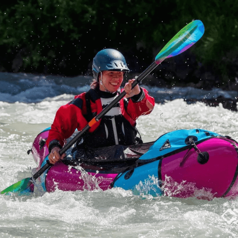 Woman paddling a pink and blue kayak through rough waters.