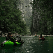 Two people in inflatable rafts navigating a river through a lush, forested canyon.