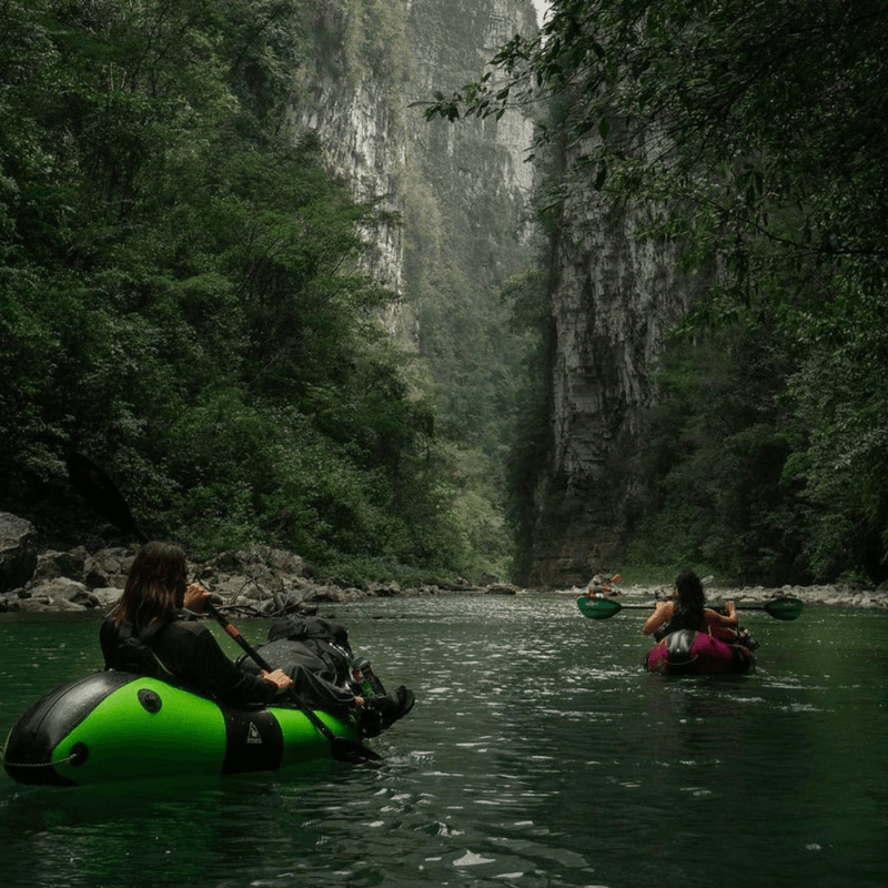Two people in inflatable rafts navigating a river through a lush, forested canyon.