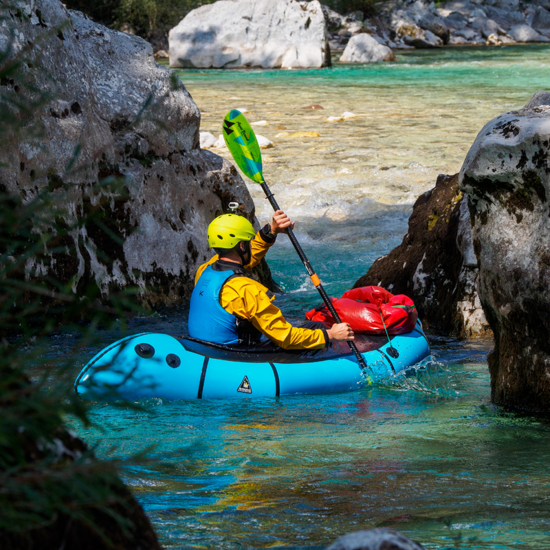 Person in a blue inflatable kayak paddling through a pair of rocks in a river.