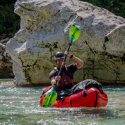Man in a red inflatable kayak paddling through calm water with a big rock in the background.