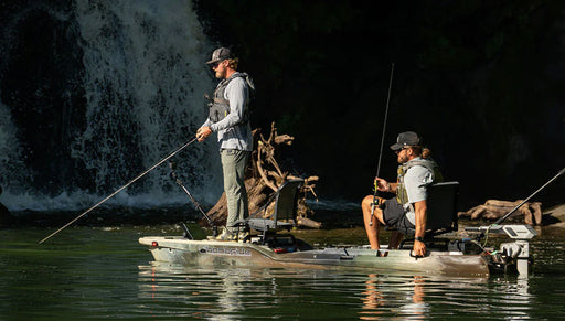 Two men on a green camouflage fishing kayak floating near a cave.