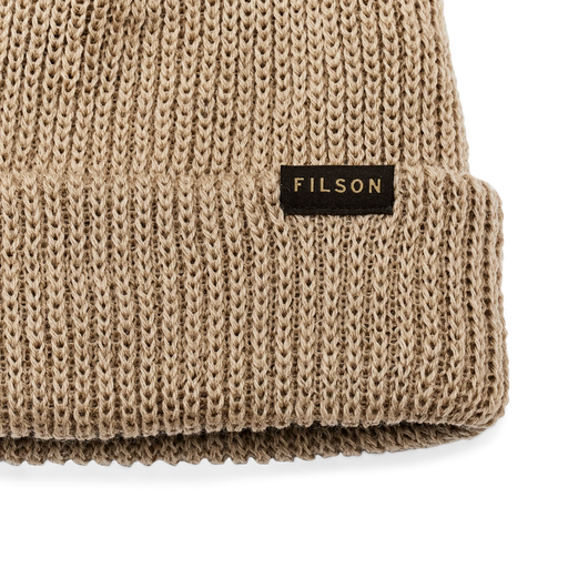Close up of a sawdust brown beanie with a tan Filson logo on it against a white background. 