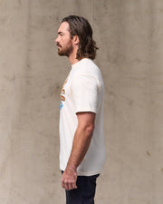 Man wearing a white t-shirt with a graphic design against a beige wall