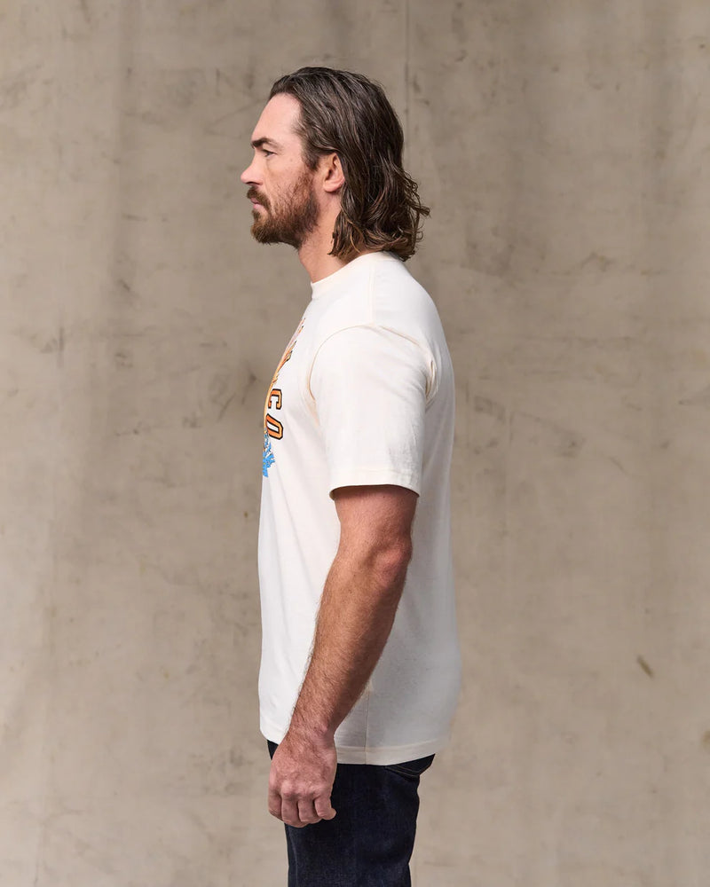 Man wearing a white t-shirt with a graphic design against a beige wall