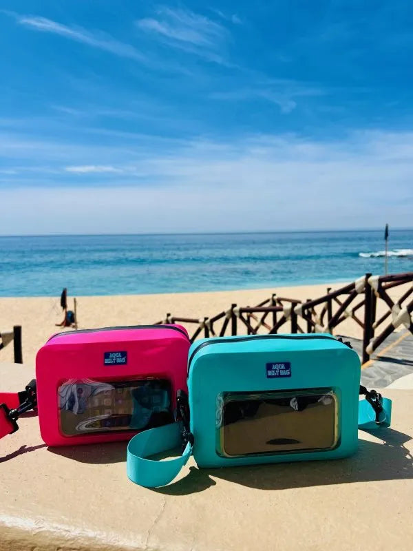 Pink and blue waterproof belt bags next to each other on a stone wall at a beach. 