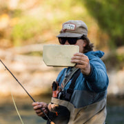 Person holding a beige cooler with 'Atollas' branding outdoors near water