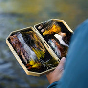 Box of fly fishing lures held by a person with a blurred natural background