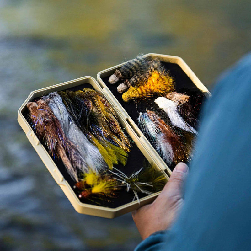 Box of fly fishing lures held by a person with a blurred natural background