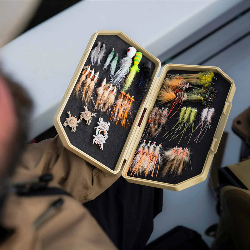 Fishing fly box with various flies held by a person outdoors.