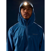 A man wearing a blue Marmot hooded jacket with a front zipper, photographed against a dark background with a headlamp on.