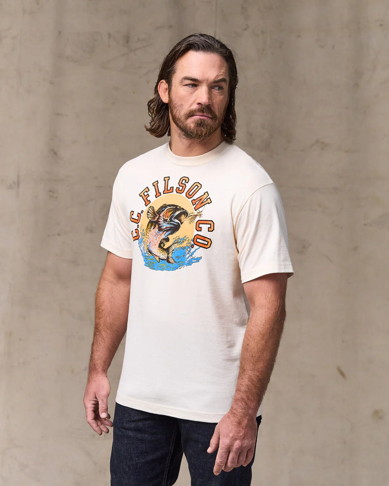 Man wearing a white t-shirt with a graphic design against a textured beige wall
