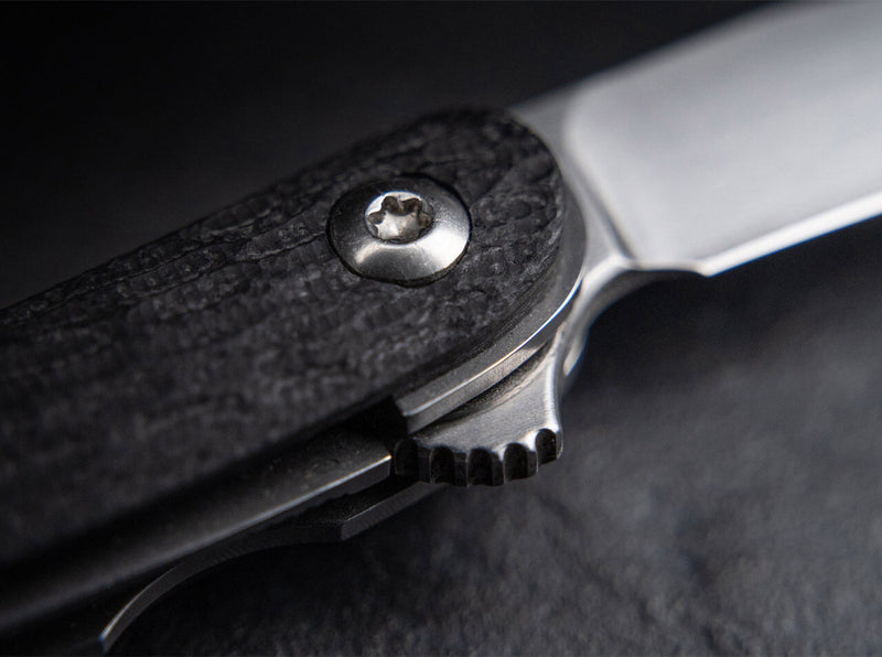 Close up image of a black knife handle as well as the closing mechanism on a black background.