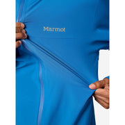 Close-up of a person wearing a bright blue Marmot jacket, pulling the fabric to show its stretch, with the Marmot logo visible on the chest.