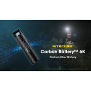 A Nitecore Carbon Battery 6K carbon fiber flashlight battery shown at an angle against a dark outdoor night scene with a faint figure holding a light source, plus large product text reading 'NITECORE Carbon Battery 6K' and 'Carbon Fiber Battery'.