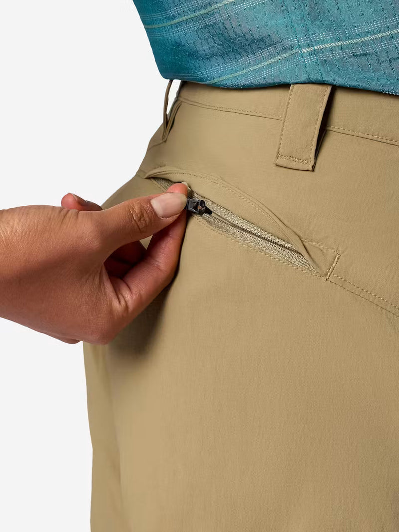 A person wearing tan cargo shorts unzipping the back pocket on a white background