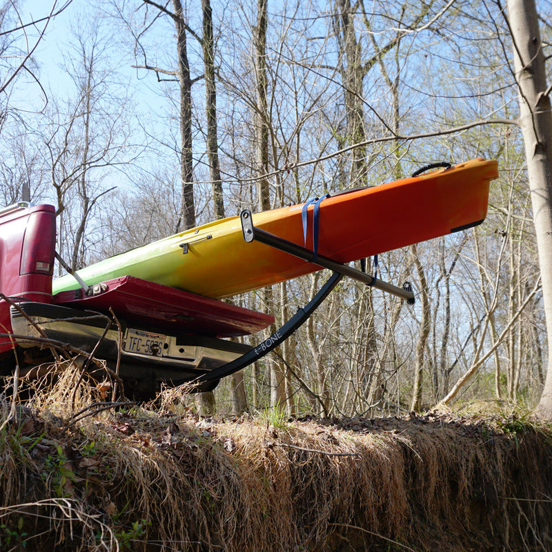 Black boat extender holding up an orange boat over an embankment in a forest.