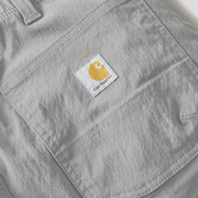 The Carhartt logo on a pair of gray cargo pants on a white background