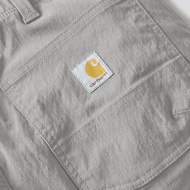 The Carhartt logo on a pair of gray cargo pants on a white background