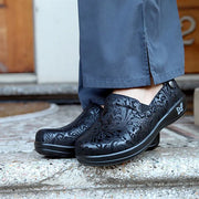 Black patterned shoes worn with blue pants on a concrete surface.