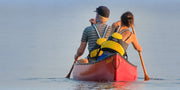 Back view of a man and a woman paddling their red canoe through calm waters.