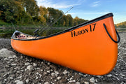 Side view of an orange canoe with a fishing pole sticking out of it on a rocky shoreline with trees in the background.