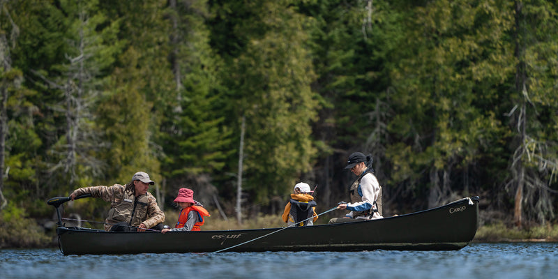 A family sitting in a black colored canoe on a lake fishing. 