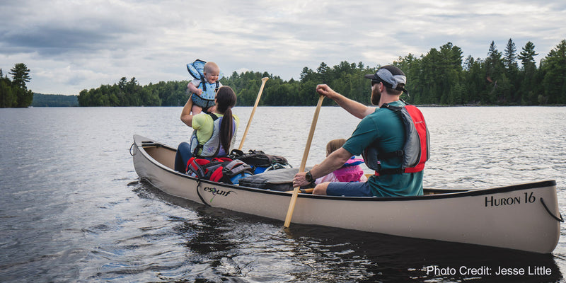 Family rowing down a calm looking river in a canoe with a Huron 16 logo on the side.