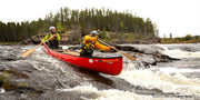 A man and a woman paddling their bright red kayak through choppy water with tall trees in the background.