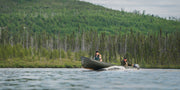 A man and a woman riding in their motor powered canoe on a lake with a scenic vista in the background.