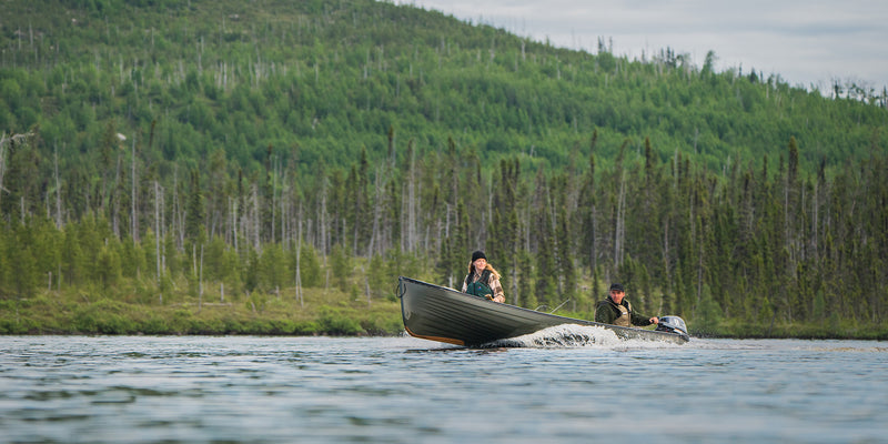 A man and a woman riding in their motor powered canoe on a lake with a scenic vista in the background.