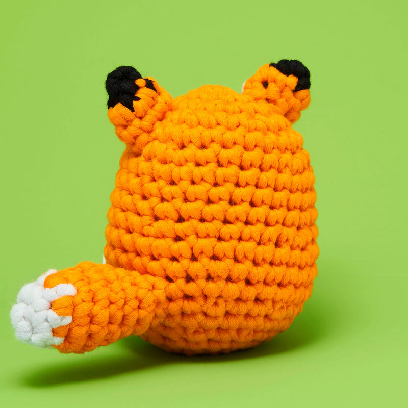Back view of a crocheted fox plushy against a green background. 