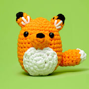 Front view of an adorable crocheted fox plushy against a green background. 
