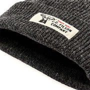 Close up of the cuff of a dark gray beanie with a Filson logo against a white background. 