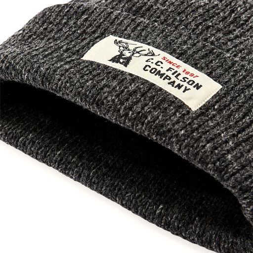 Close up of the cuff of a dark gray beanie with a Filson logo against a white background. 