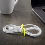 White cable with a yellow tie on a dark surface next to a laptop and mug