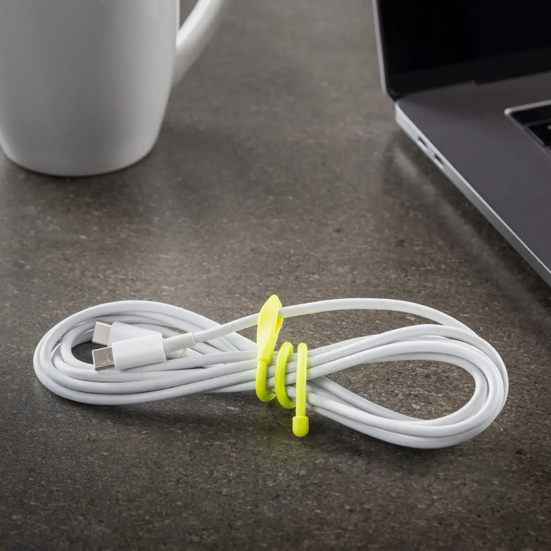 White cable with a yellow tie on a dark surface next to a laptop and mug