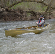 Man paddling a canoe on a river with trees and rocks in the background