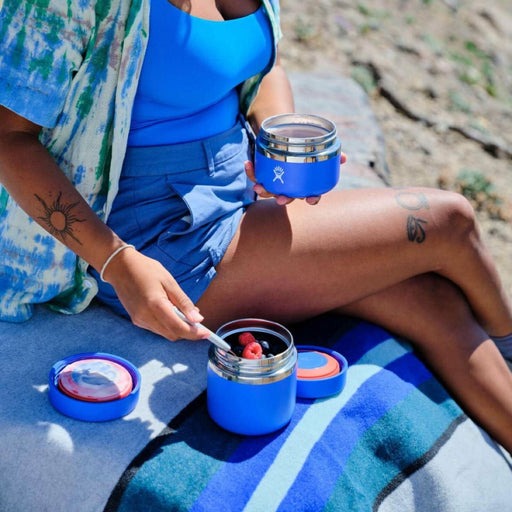 Person sitting outdoors with blue containers and a spoon